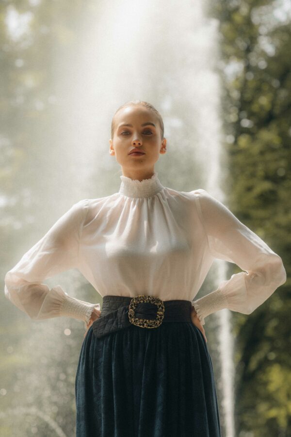 Frauenmodel mit hochgeschlossener weißen Bluse und gemustertem Rock in dunkelblau